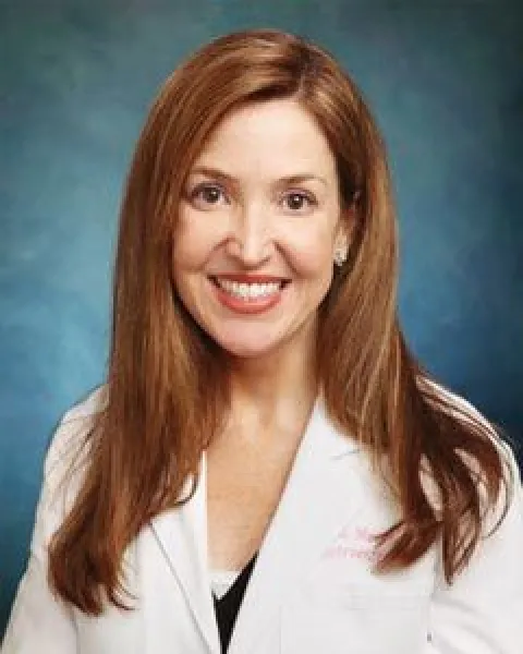 A portrait of A portrait of Angela M. Meyer, MD, smiling in a white coat posed for a portrait against a blue backdrop.