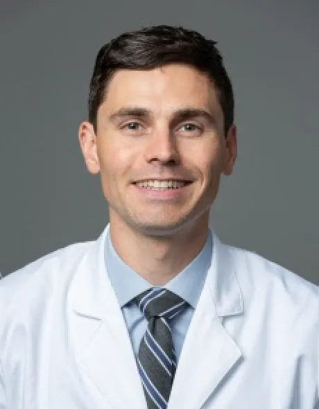 Brendon O’Connell, MD, in a white lab coat and striped tie smiling at the camera (portrait headshot).