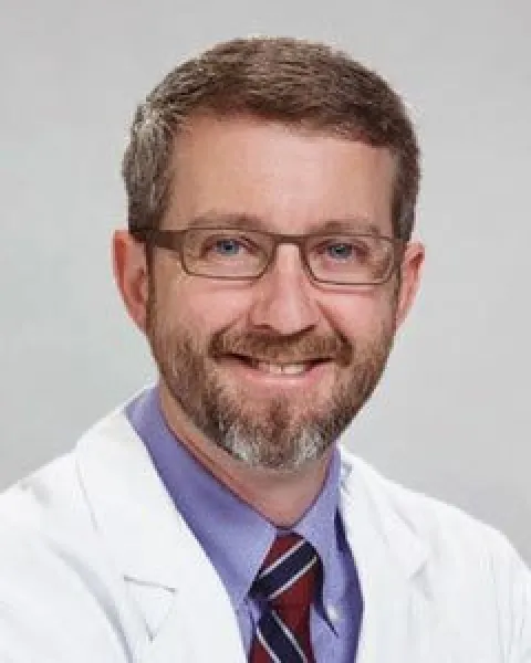 Brian Garvin, MD, smiling in a white coat, purple shirt, and striped tie looking at the camera.