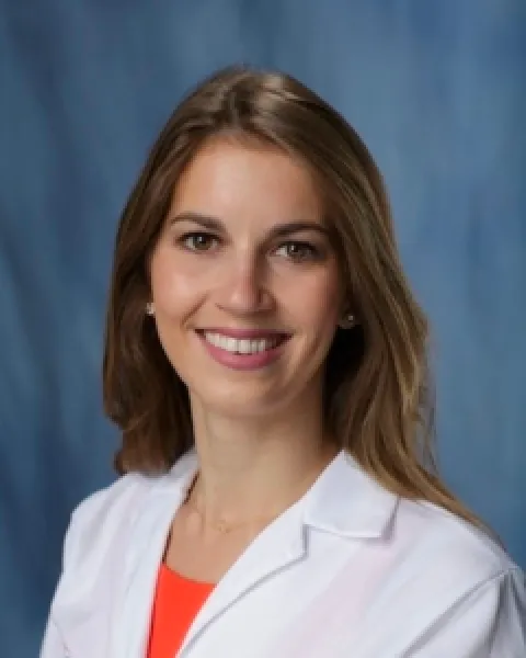 Head-and-shoulders portrait of Chelsea Jacobs, DO, smiling in a white lab coat against a blue background.