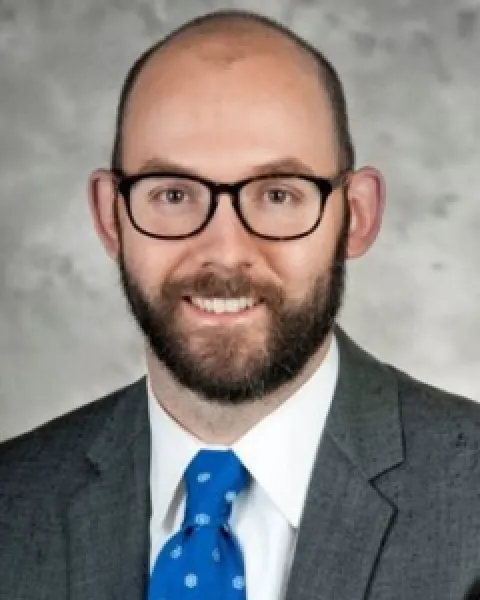 Professional headshot: David A. Rybnicek, MD, wearing a gray suit and blue tie, smiling at the camera.