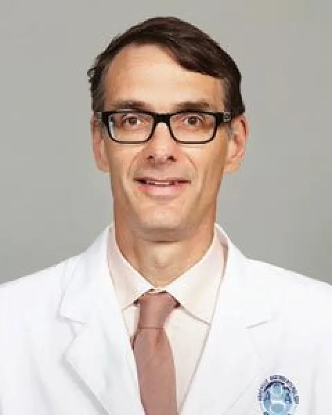 David T. May, MD, smiling in a white coat and pink tie, wearing glasses, facing the camera.