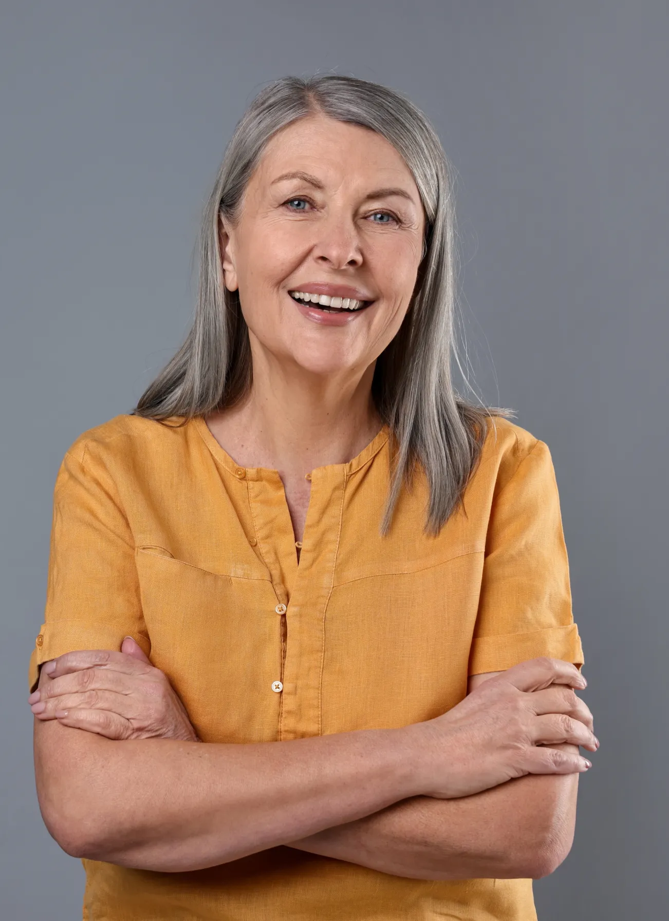 Smiling older woman with gray hair wearing a mustard-yellow blouse.