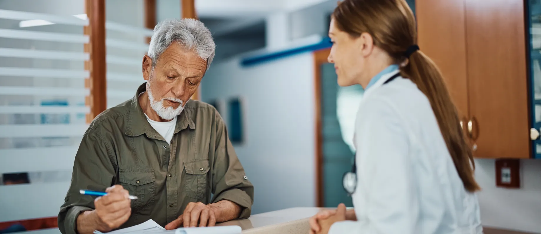 Patient completing paperwork at a clinic counter with a healthcare professional.